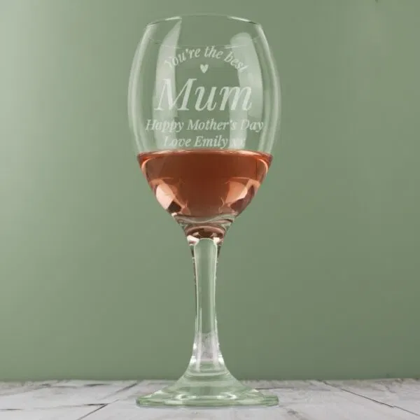 A personalised wine glass from Abode Home & Gifts filled with rosé wine against a sage green background.