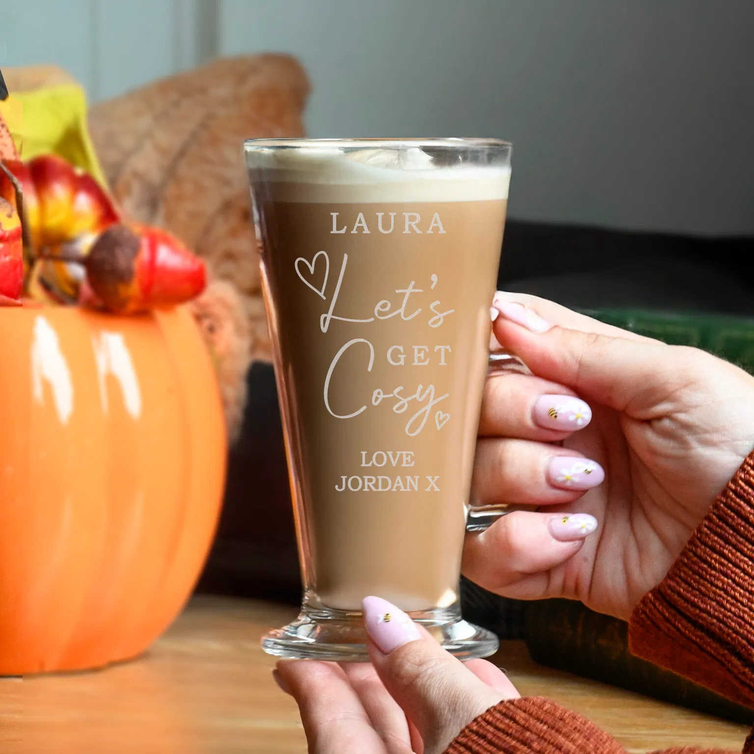 Hand holding a latte glass etched with 'Let's Get Cosy' next to a pumpkin.