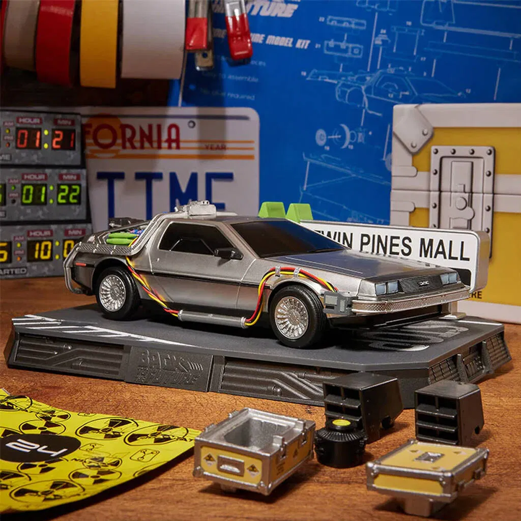 A detailed die-cast model of the silver DeLorean time machine from the movie Back to the Future is featured prominently on a black display platform. The scene is set with miniature accessories, including yellow crates and black equipment, that are presumably revealed through the advent calendar. In the background, there are digital clocks displaying times from the film, emphasising the time travel theme. The Ultimate Advent Calendar gift for Back to the Future fans and model collectors.