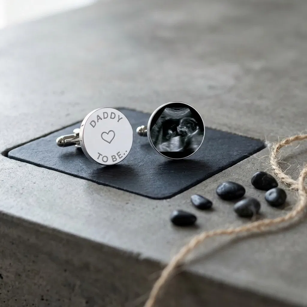 Abode Home & Gifts 'Daddy To Be' personalised baby scan cufflinks displayed on a dark slate coaster over a modern concrete counter.
