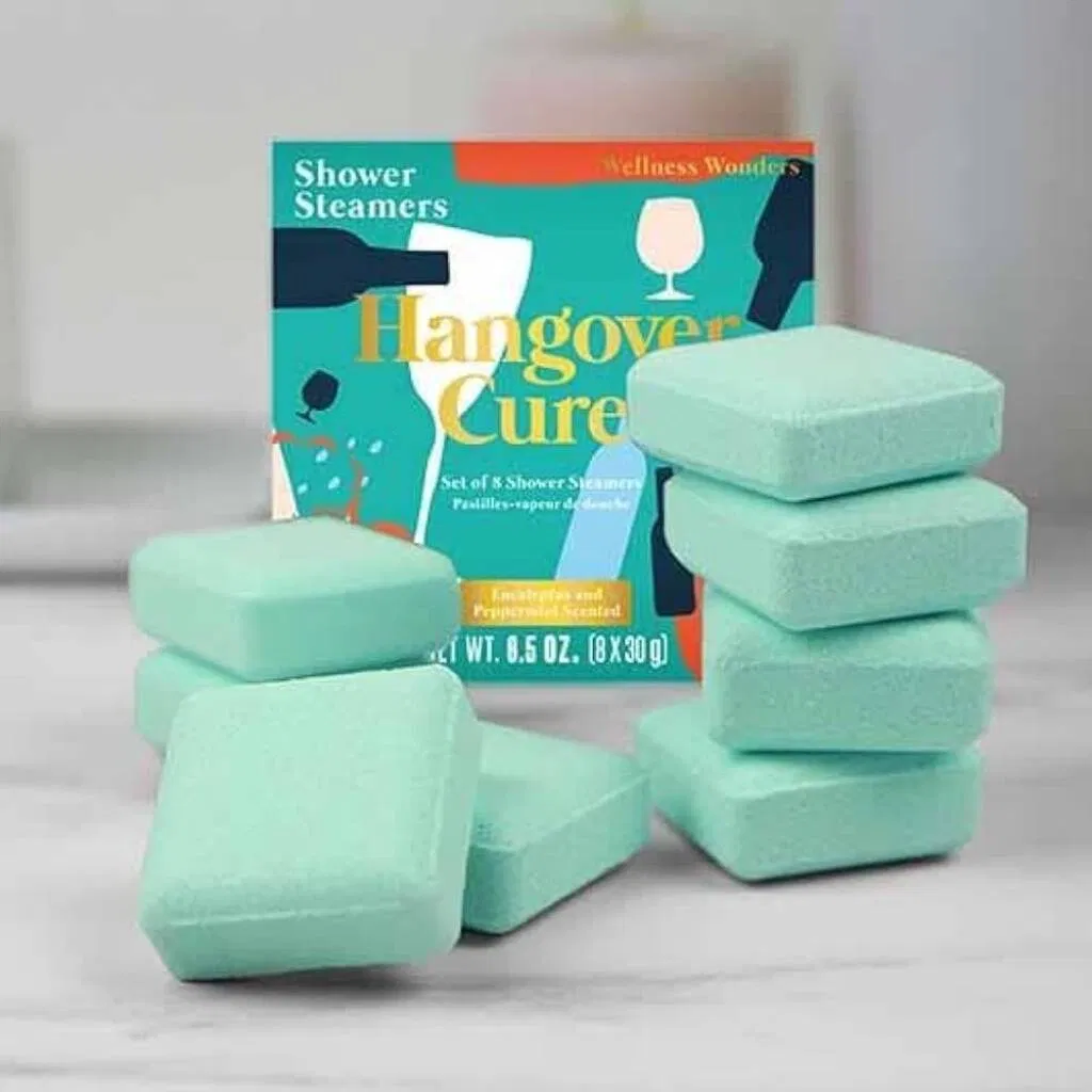 Set of 8 square green Hangover Cure Shower Steamers, scented with eucalyptus and peppermint, stacked next to the colorful 'Wellness Wonders' product box.