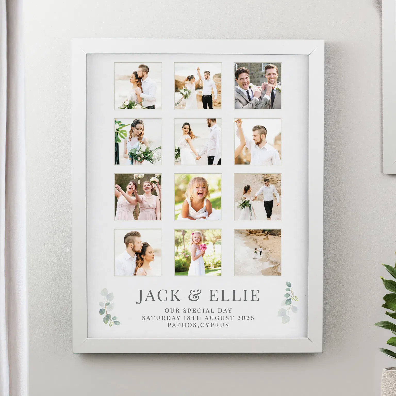 A large white 12-aperture collage photo frame by Abode Home & Gifts hanging on a wall, showcasing full-colour destination beach wedding photos. The bottom mount includes green eucalyptus leaves and printed text reading "JACK & ELLIE OUR SPECIAL DAY SATURDAY 18TH AUGUST 2025 PAPHOS, CYPRUS".