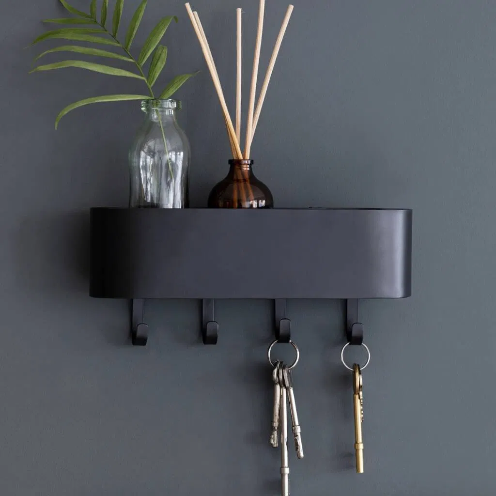 Modern wall-mounted key hook and storage shelf in a minimalist black or white design, featuring four metal hooks for keys and a top shelf holding a vase and diffuser, providing organised entryway storage.