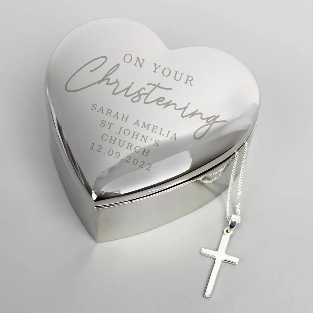 A heart-shaped, silver-plated trinket box engraved with "On Your Christening" details, shown next to a matching silver cross necklace and chain. Ideal personalised keepsake gift for a Christening, Baptism, or Holy Communion.