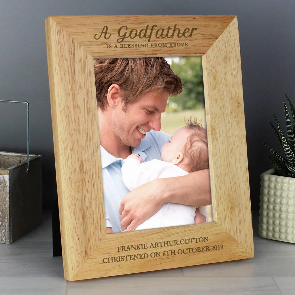 Personalised wooden photo frame engraved with the fixed text "A Godfather is a blessing from above" at the top and custom personalised text below the photo, currently showing "Frankie Arthur Cotton Christened on 8th October 2019". The frame holds a 5x7 portrait photo of a smiling man holding a baby.