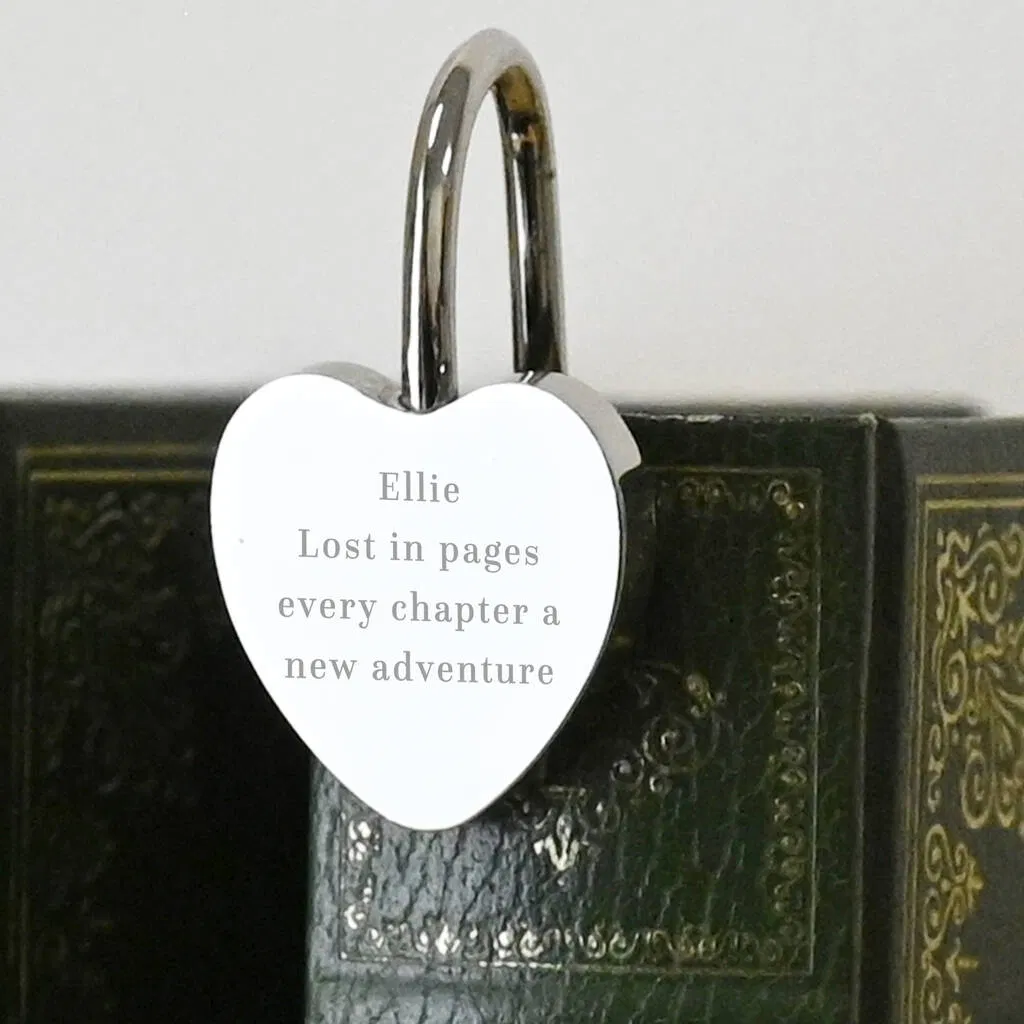 Alt Text: A luxury polished silver heart-shaped bookmark clipped onto the spine of a vintage green leather-bound book. The heart is engraved with the name "Ellie" and the sentimental quote: "Lost in pages every chapter a new adventure."