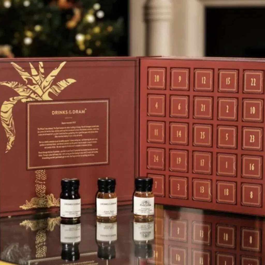 A premium Advent Calendar box featuring 24 individually labelled doors, containing a miniature bottle of spiced rum behind each one. The design is festive and sophisticated, possibly featuring gold foil or deep red coloring. Ideal luxury Christmas gift or adult countdown calendar for rum enthusiasts.