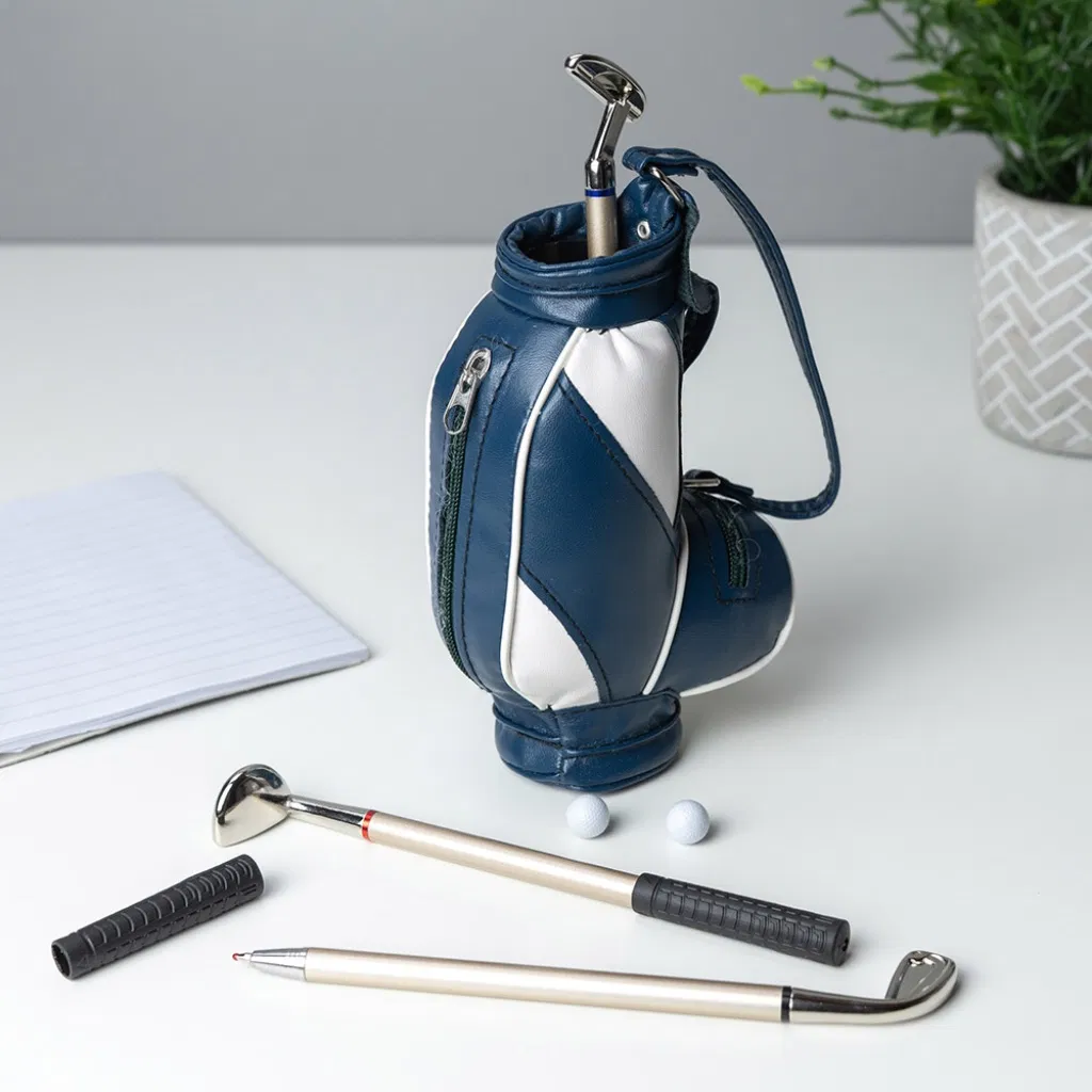Miniature golf bag desk organiser pen set in navy blue and white, holding three novelty pens shaped like golf clubs (putter and irons), displayed with two small golf balls and a notepad.