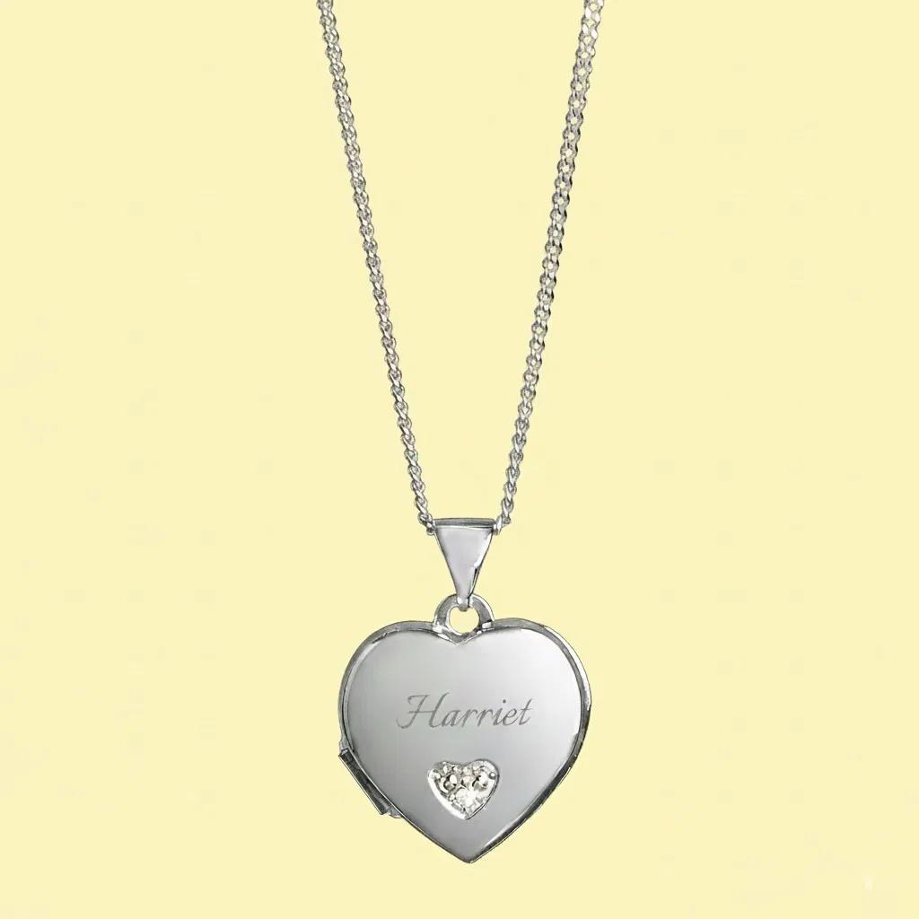 A personalised girl's heart locket necklace with a silver-toned chain, featuring an engraved first name ("Harriet") and a small diamond-shaped crystal heart detail on the front, hanging against a solid pastel yellow background.