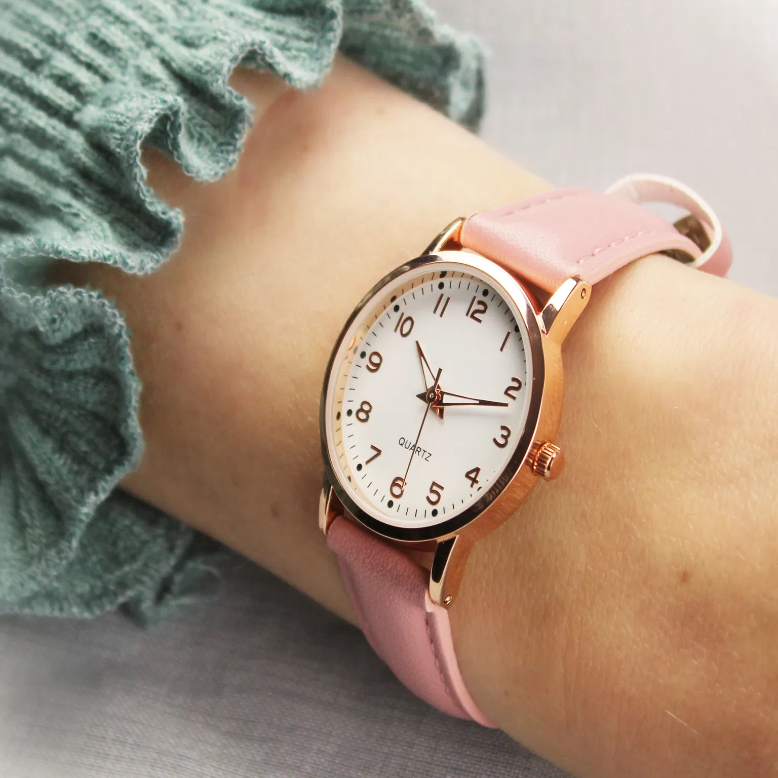 Close-up of a girl's arm wearing a personalised watch with a pink or floral fabric strap and a clear white dial, featuring large, easy-to-read numbers, ideal for teaching time.