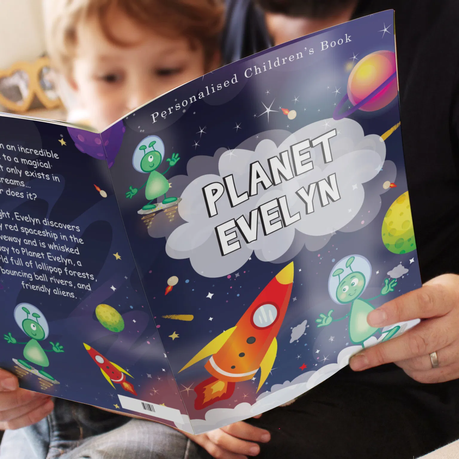 A close-up image of a person holding an open, colorful children's book titled "Planet Evelyn." The cover features a red and yellow rocket ship, green friendly aliens, stars, and planets against a dark, starry space background. A child with blonde hair is blurred in the background, leaning in to read the book with the adult. Text on the open page describes Evelyn's journey to a magical world full of lollipop forests and friendly aliens.
