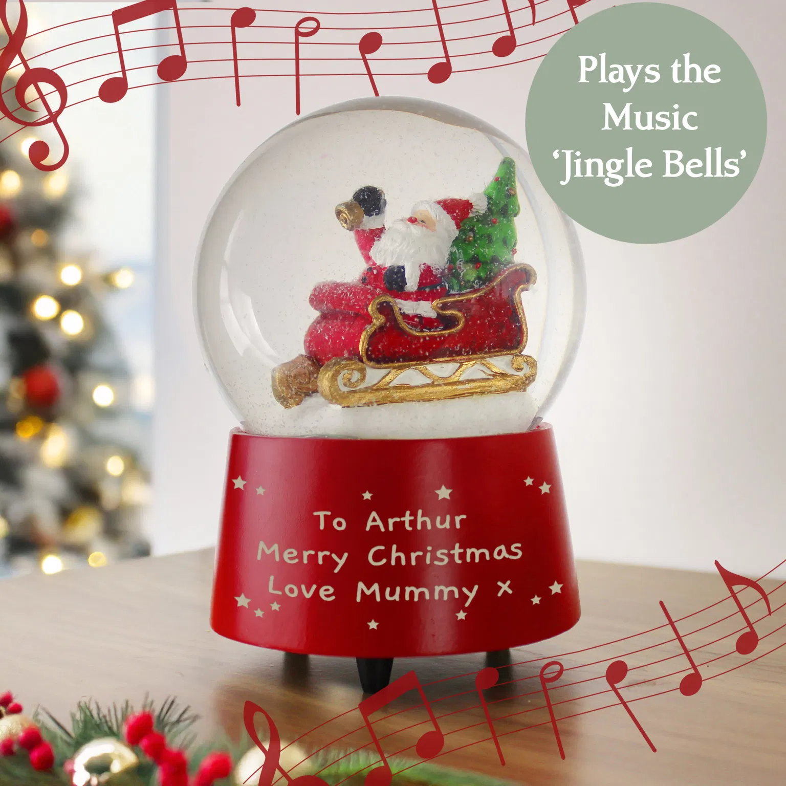 A personalised musical Santa snow globe with a red base, featuring a figure of Santa Claus in his sleigh next to a Christmas tree inside, and the custom engraved message 'To Arthur Merry Christmas Love Mummy' on the base, which plays the music 'Jingle Bells'.