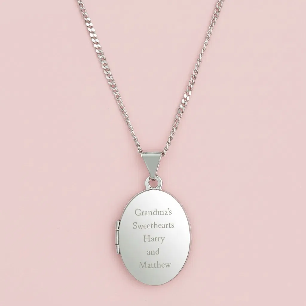 Close-up of the back of a polished sterling silver oval locket necklace, showing the custom engraved message 'To Mummy With Love & Kisses From Ida x' on a pink background.