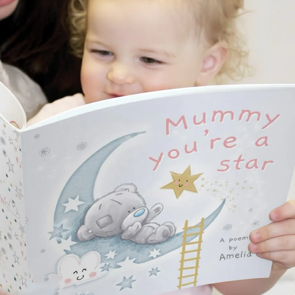 A young child holding an open personalised 'Mummy You're A Star' poem book. The cover features an adorable Tiny Tatty Teddy sleeping on a crescent moon among stars and clouds, with the title in soft pink lettering.