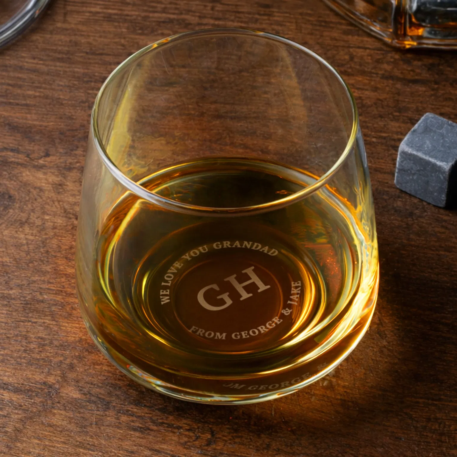 Glass whisky tumbler viewed from above showing custom base engraving that reads 'GH - WE LOVE YOU GRANDAD FROM GEORGE & JAKE'.