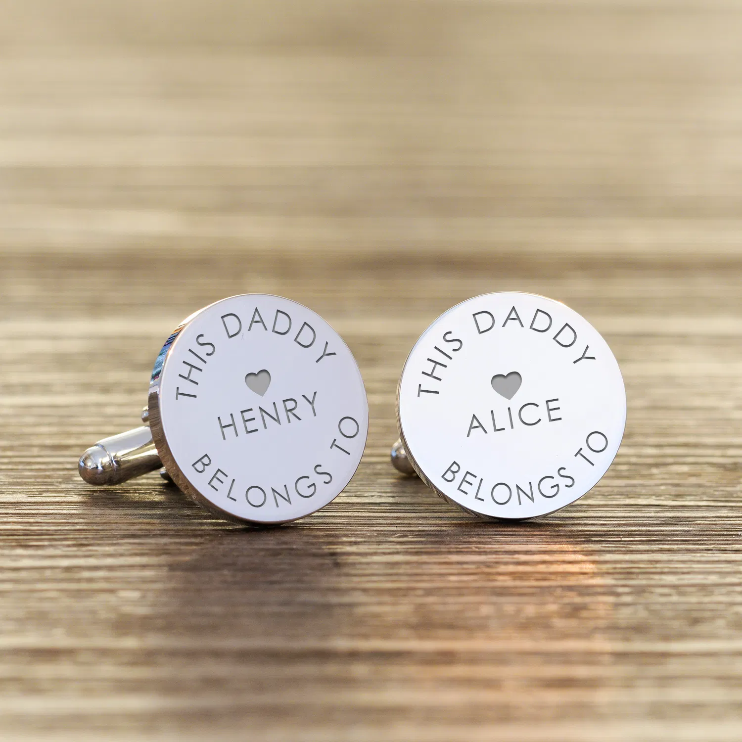 Pair of polished round silver cufflinks engraved with 'THIS DADDY BELONGS TO' and the names Henry and Alice, displayed on a textured wooden surface.