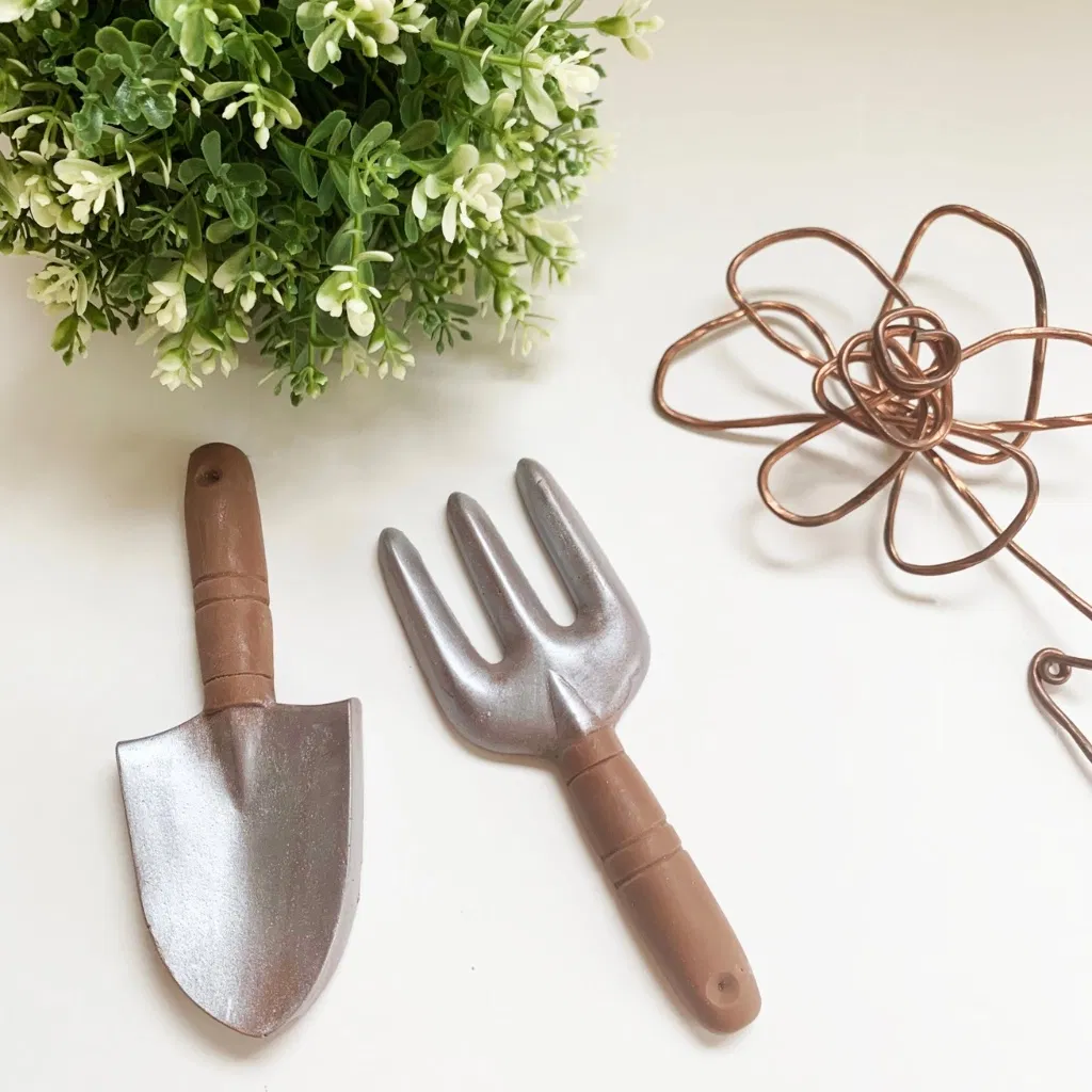 Novelty Chocolate Garden Tools: A realistic chocolate trowel and garden fork with silver-lustre "metal" finishes and chocolate brown handles. Shown on a white surface next to a decorative plant.