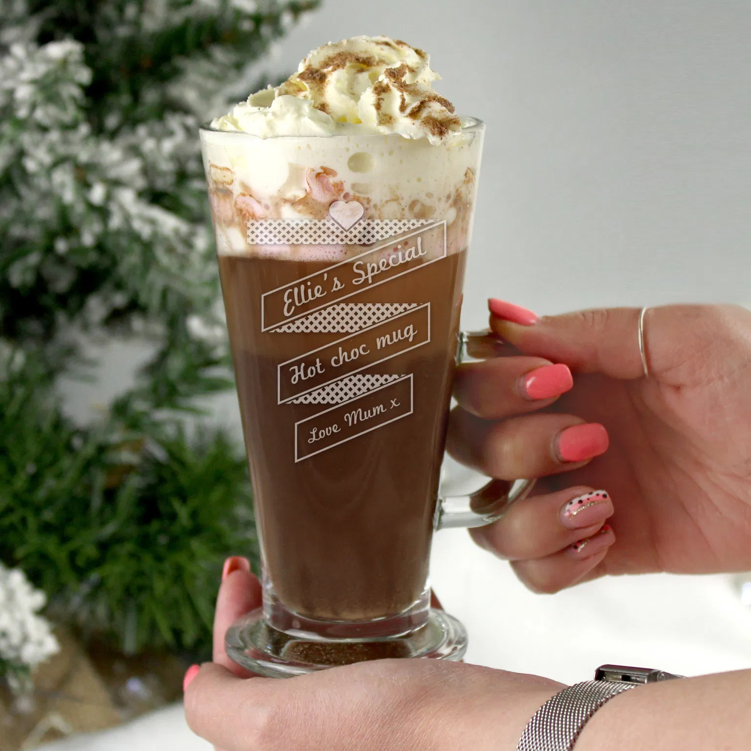 A person holding an elegant latte glass filled with hot chocolate and whipped cream, featuring a heart banner design and the text "Ellie's Special," "Hot choc mug," and "Love Mum x."
