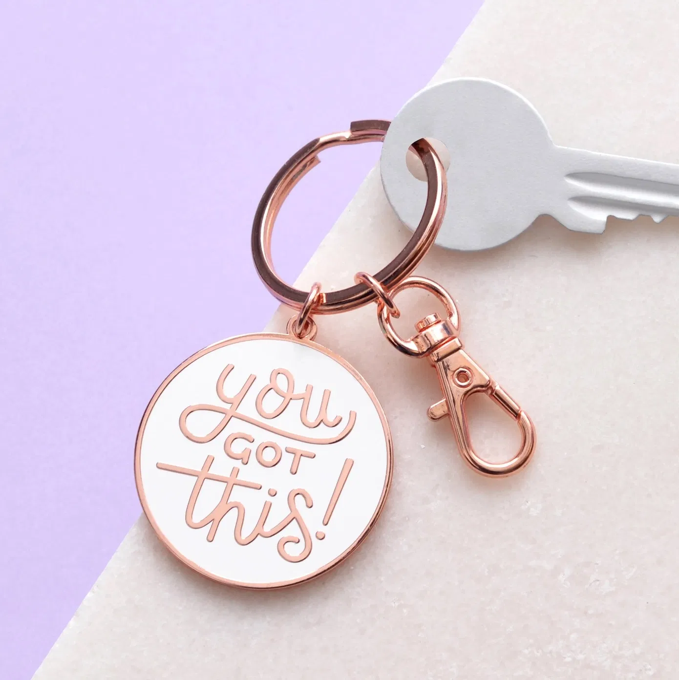 A white enamel keyring with copper trim featuring the handwritten text You Got This. The keyring has a split ring and a lobster clasp, resting on a soft-textured background.