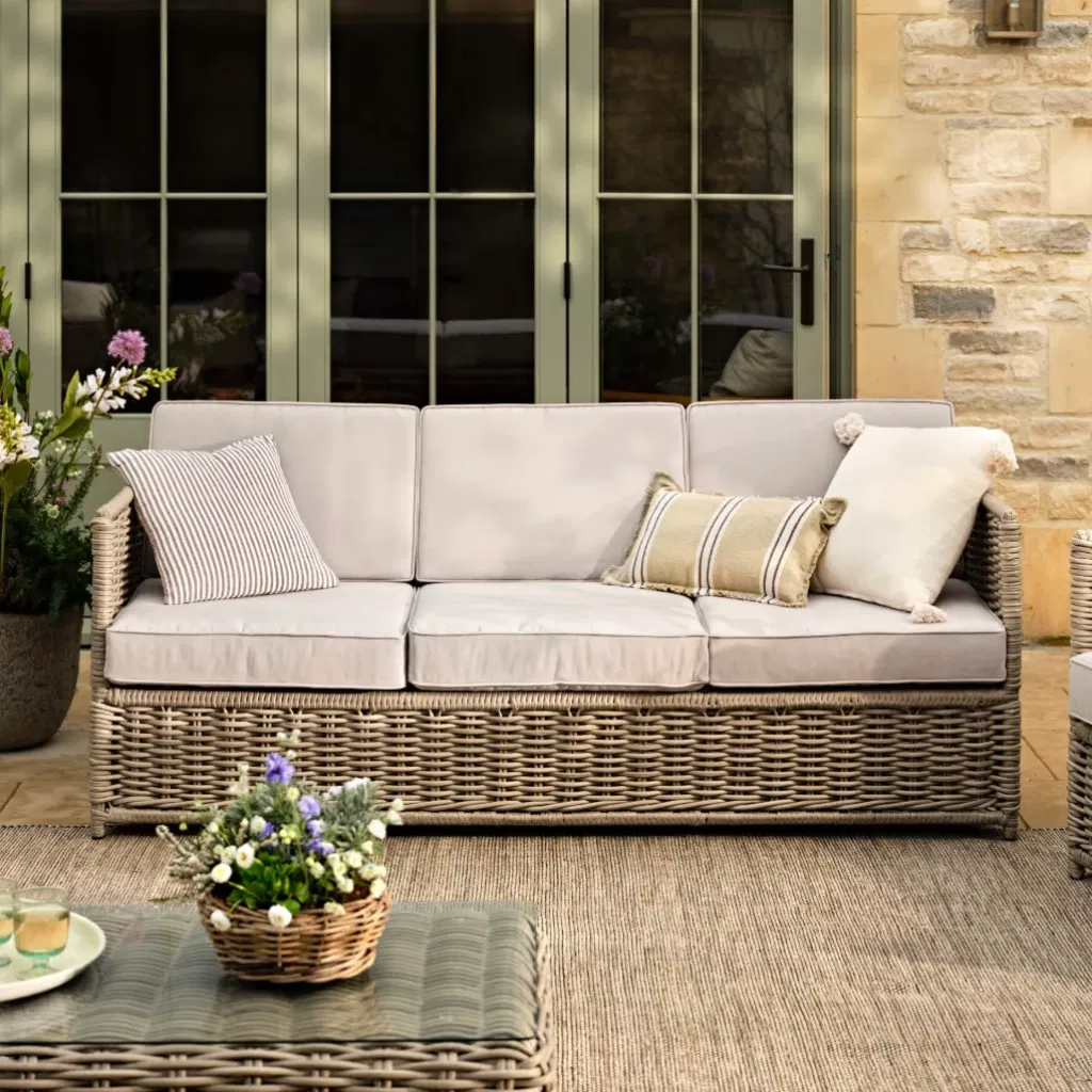 Stone-coloured rattan 3-seater sofa with neutral cushions on a patio.