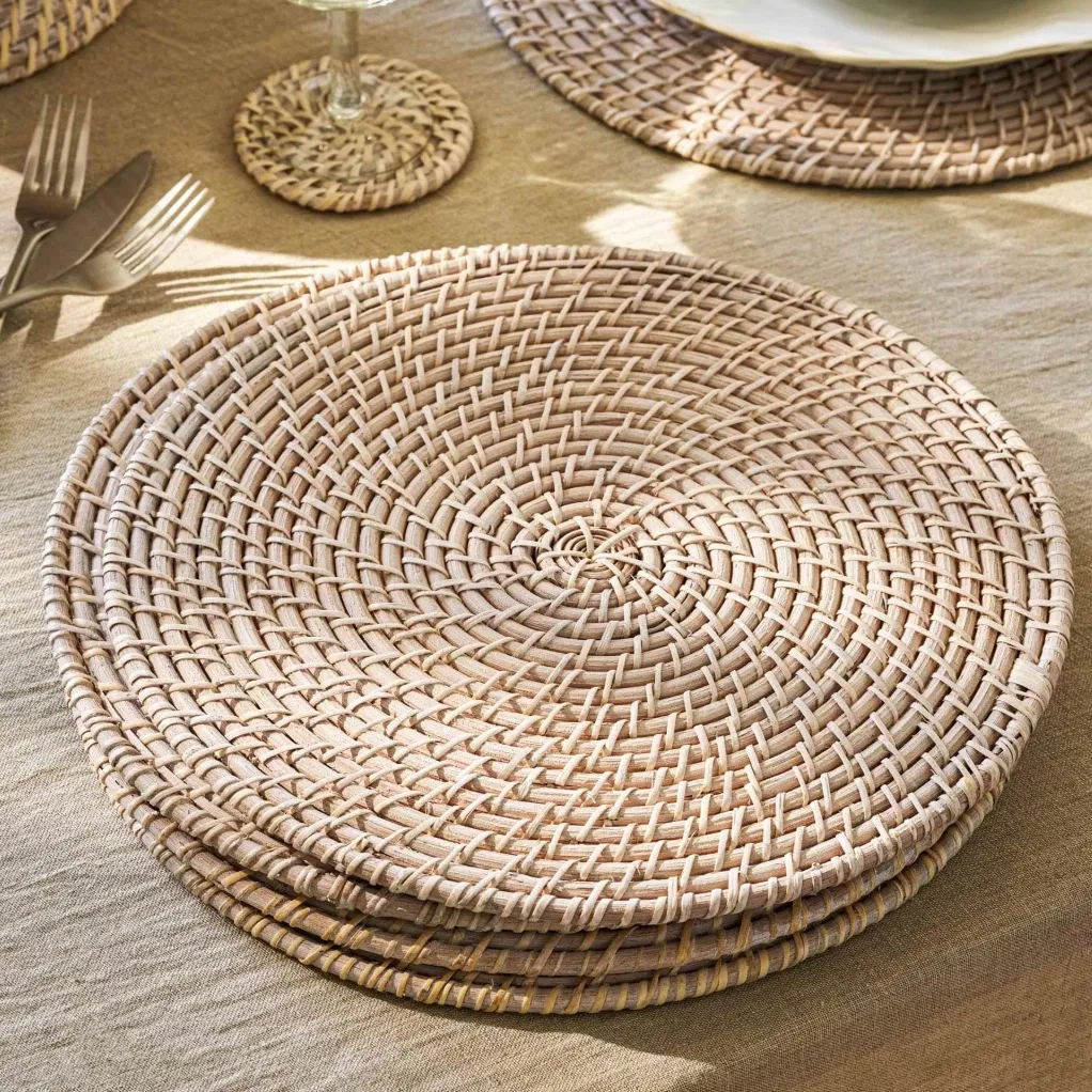 Set of 4 round whitewash rattan placemats styled on a linen tablecloth with glassware.
