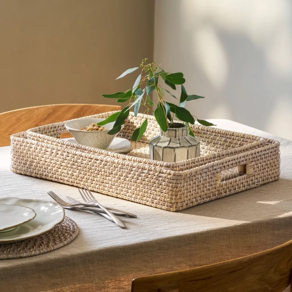 Set of two nesting rectangular whitewash rattan trays styled on a dining table with a vase.