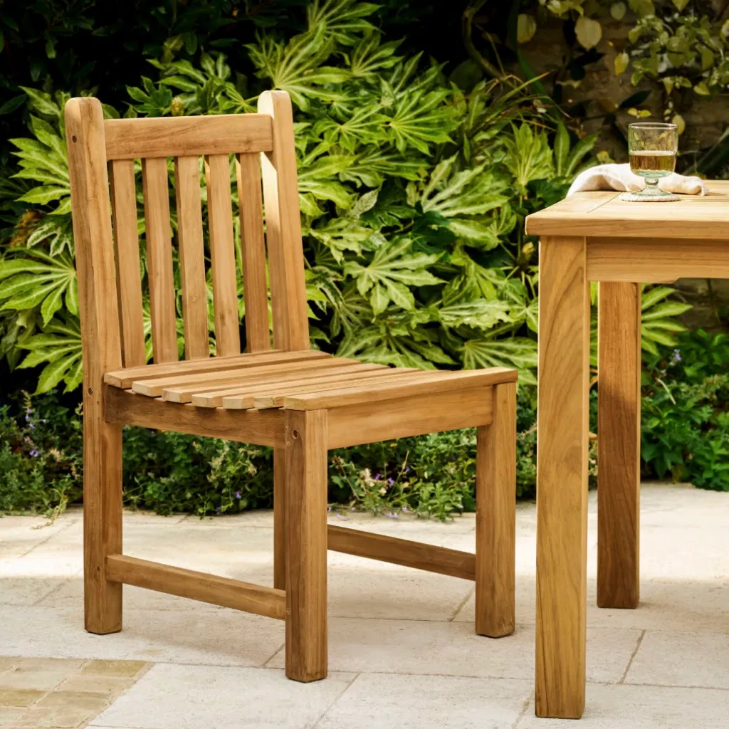 Front-angled view of a solid teak garden armchair with a multi-slatted back on a stone patio.