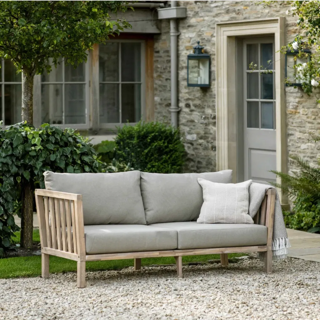 Traditional 2-seater garden sofa in whitewash acacia wood with soft grey cushions on a gravel patio.
