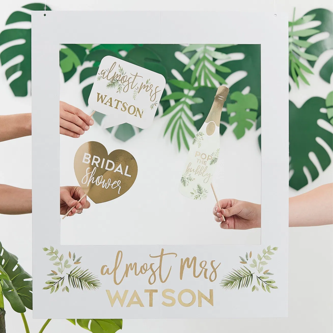 Hands holding a white botanical hen party photo frame personalised with gold text reading almost Mrs WATSON alongside matching handheld photo props.