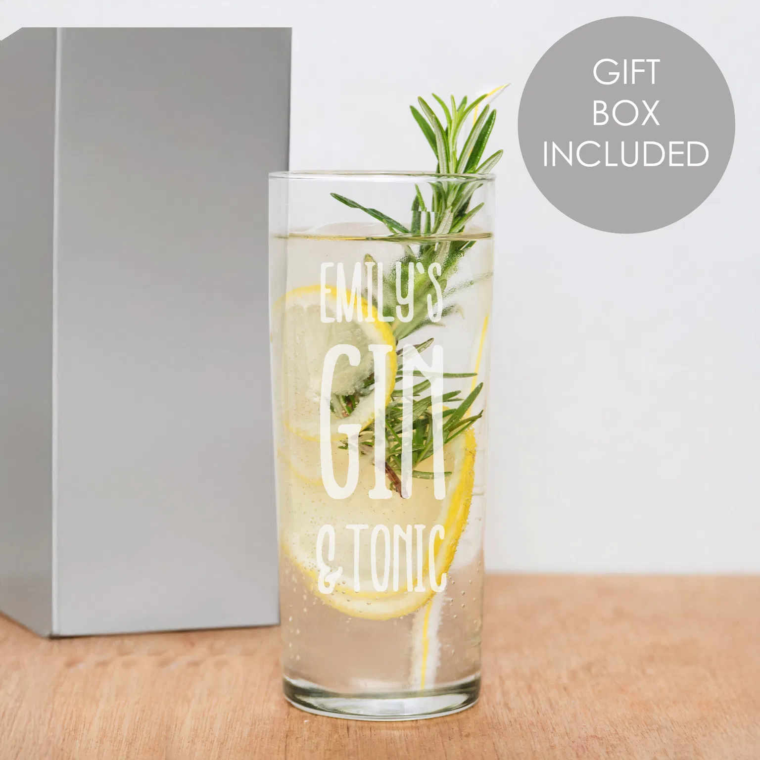 A personalised hi ball glass by Abode Home & Gifts, filled with an iced gin drink and a lime slice garnish, featuring the custom engraved text "EMILY'S GIN & TONIC" in bold block capitals, set against a dark grey stone backdrop next to a bottle of tonic water.