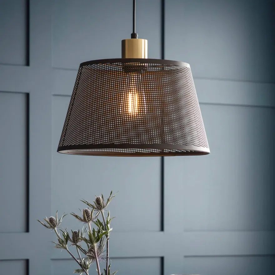 A single black steel mesh pendant light with a brushed brass fitting illuminated against a textured grey background by Abode Home & Gifts.