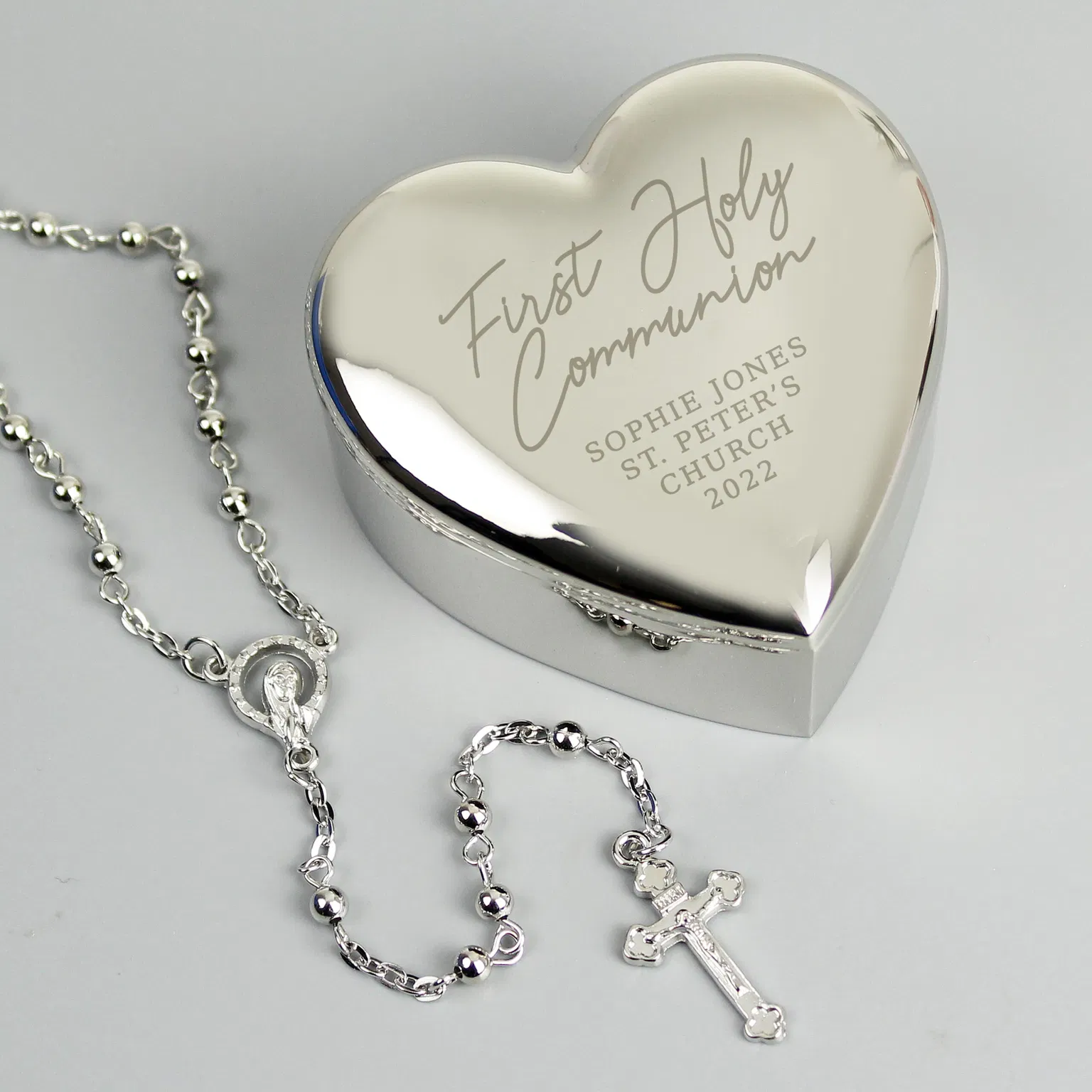 Personalised nickel-plated heart trinket box engraved with First Holy Communion details next to matching silver rosary beads.