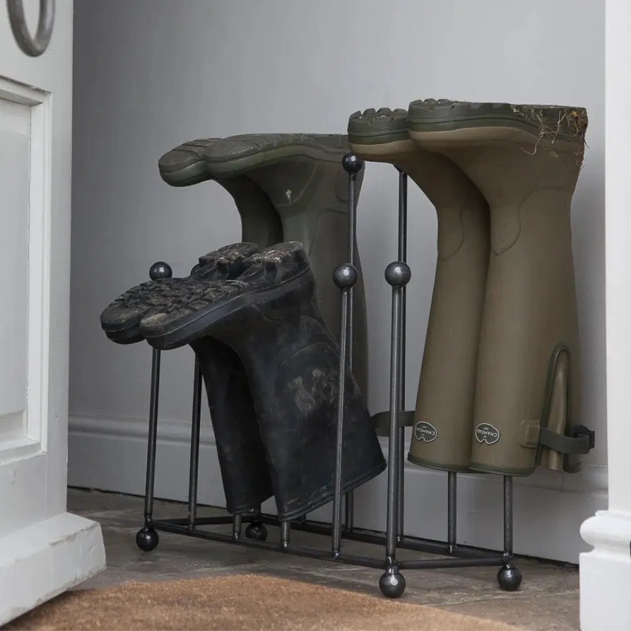 A raw metal dark grey welly stand holding green and black boots inside an entryway by Abode Home & Gifts.