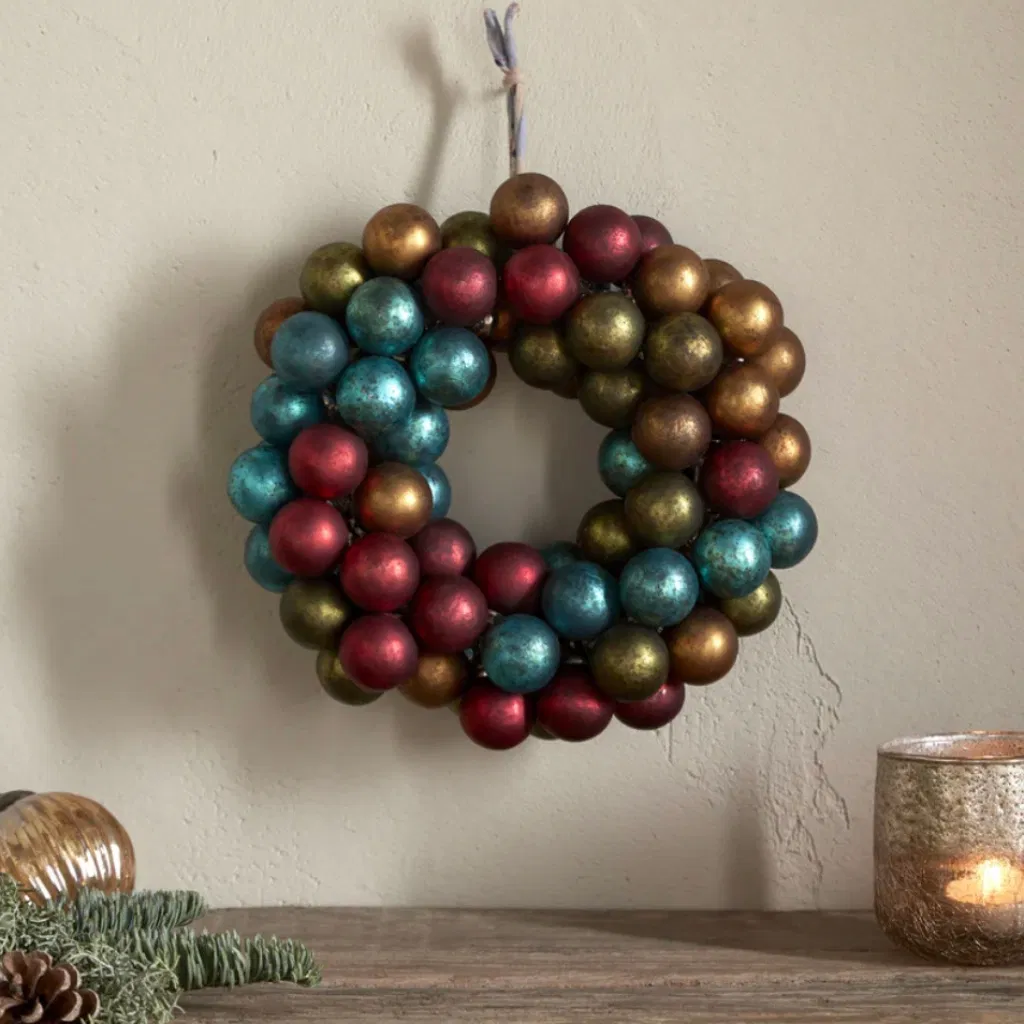 Recycled glass bauble wreath hung on a wall above a rustic wooden shelf with a flickering candle.