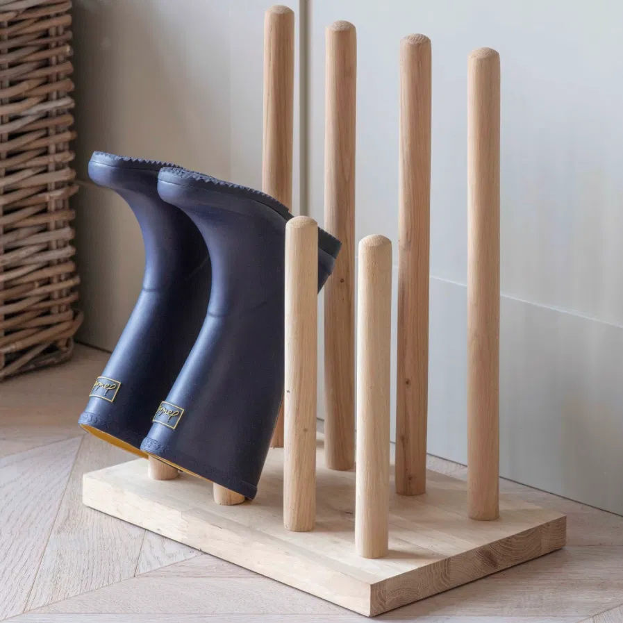 A solid oak welly stand holding various pairs of rubber wellington boots inside an entryway by Abode Home & Gifts.