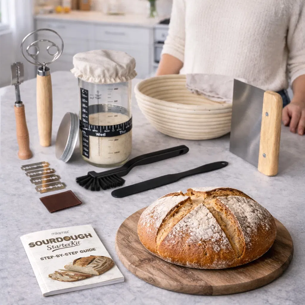 Complete sourdough starter kit with glass jar, dough whisk, proofing basket, bench scraper, and a fresh loaf of bread on a table.