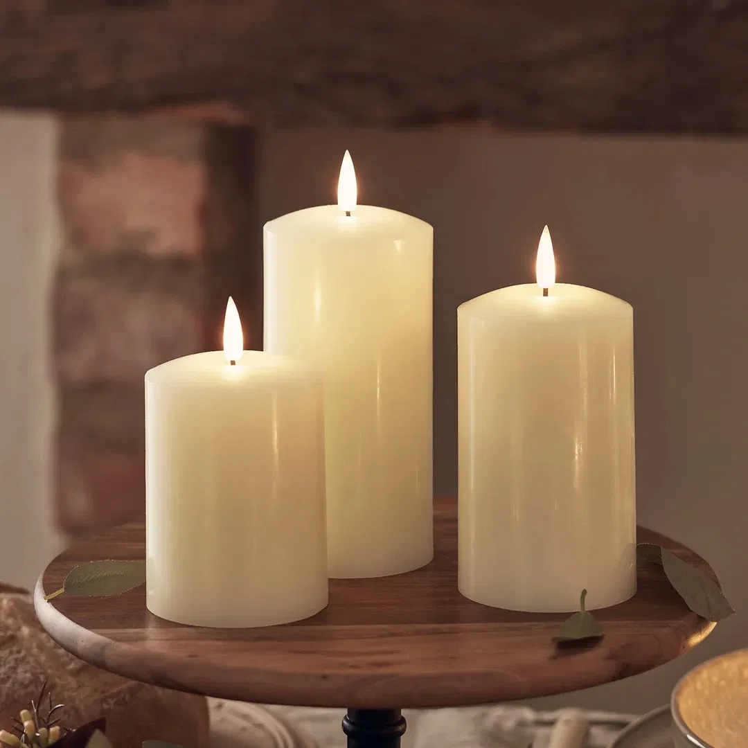 Staggered trio of TruGlow ivory rechargeable LED pillar candles with flickering flames on a white background.